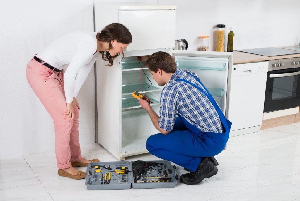 Male Worker Repairing Refrigerator In Kitchen Room
