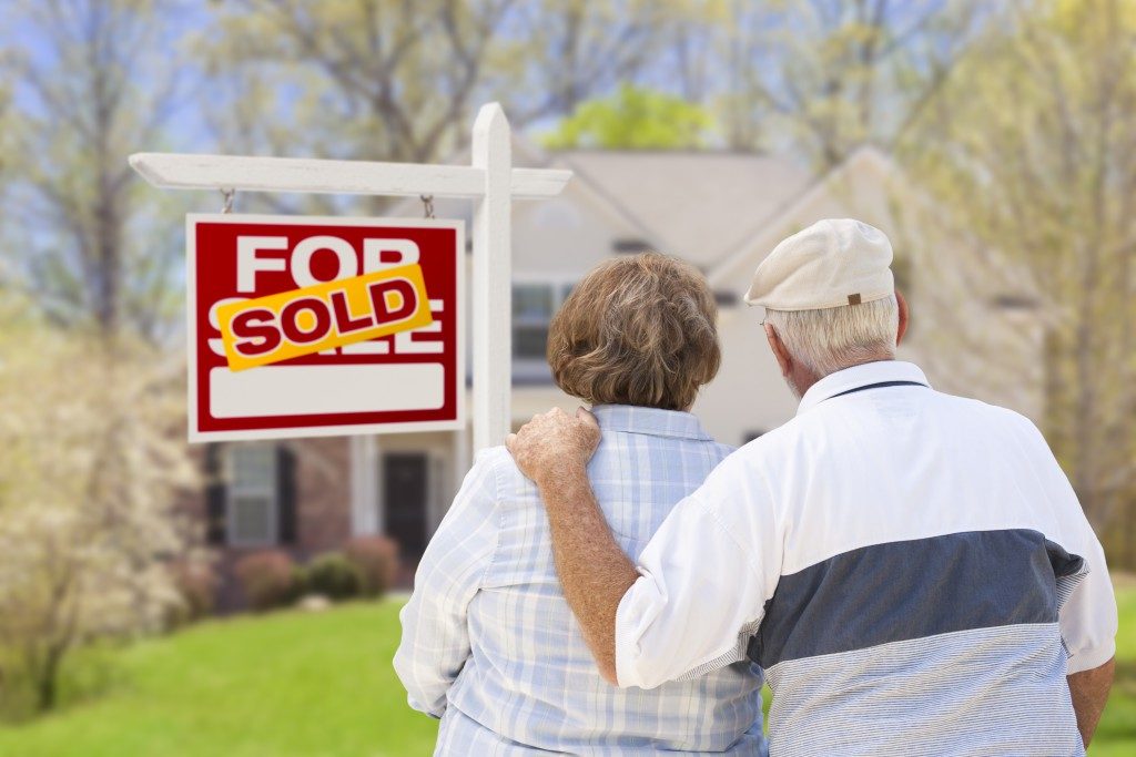 Senior Couple Hugging in Front of Sold Real Estate Sign and House
