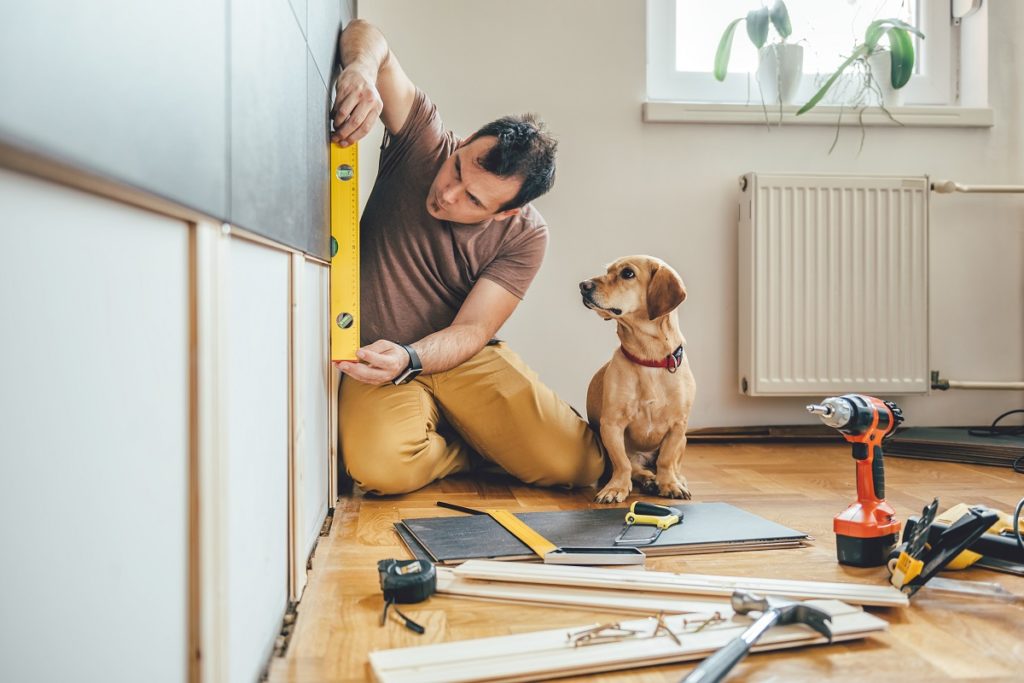 Man measuring wall with dog beside him