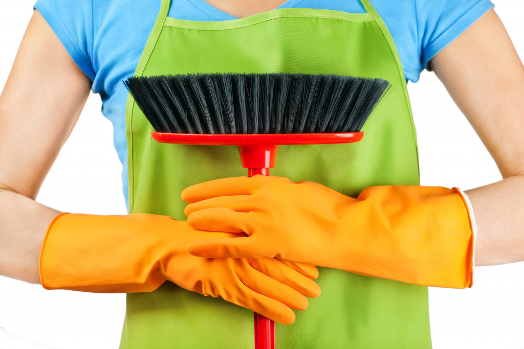 Woman wearing apron and gloves while holding a broom